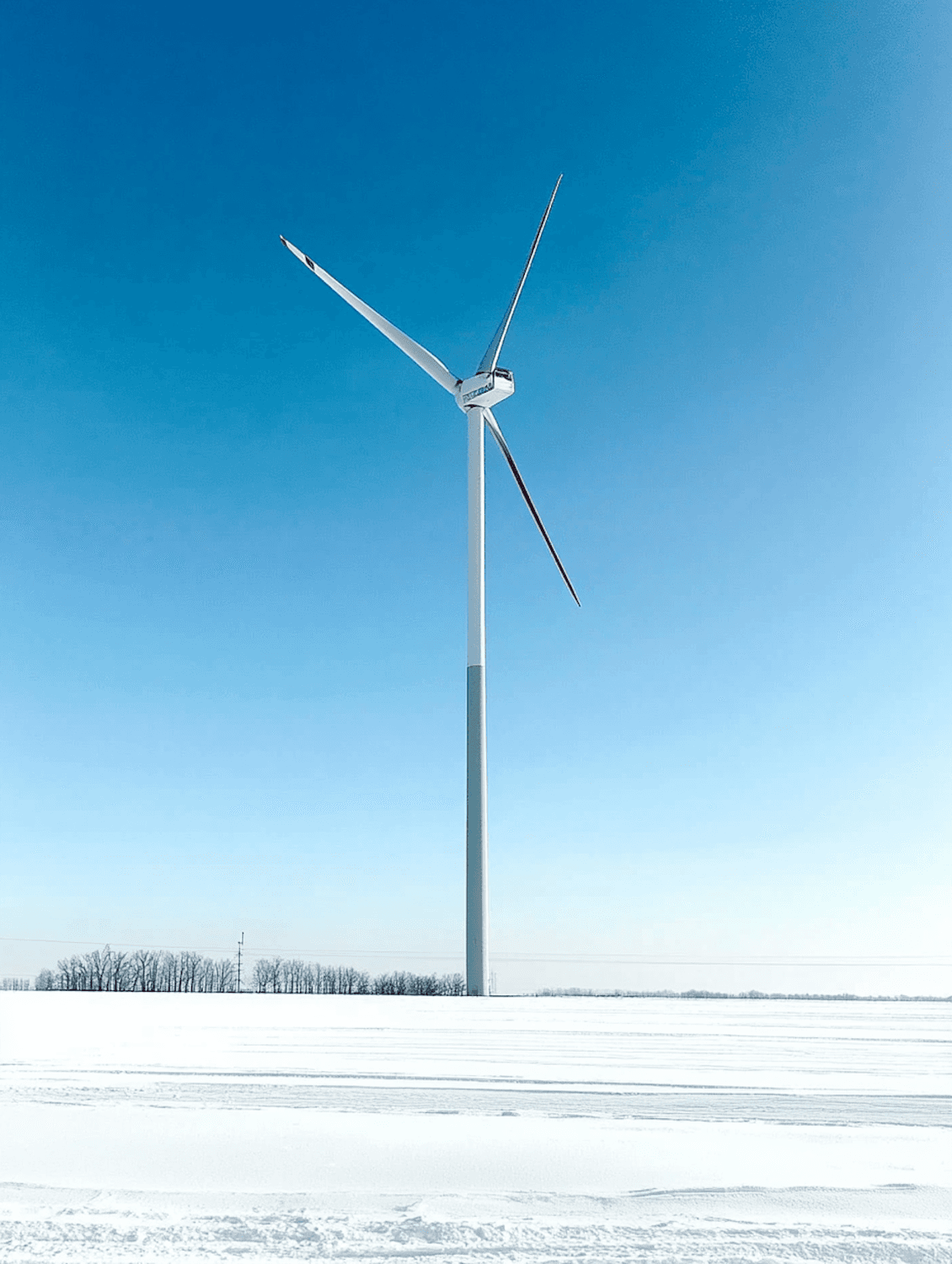 A wind turbine standing in a snowy landscape under a clear blue sky